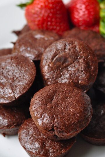 round 2 bite brownies on white plate with 2 whole strawberries in background