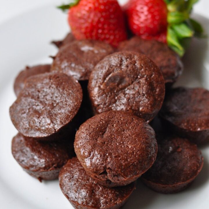 round 2 bite brownies on white plate with 2 whole strawberries in background
