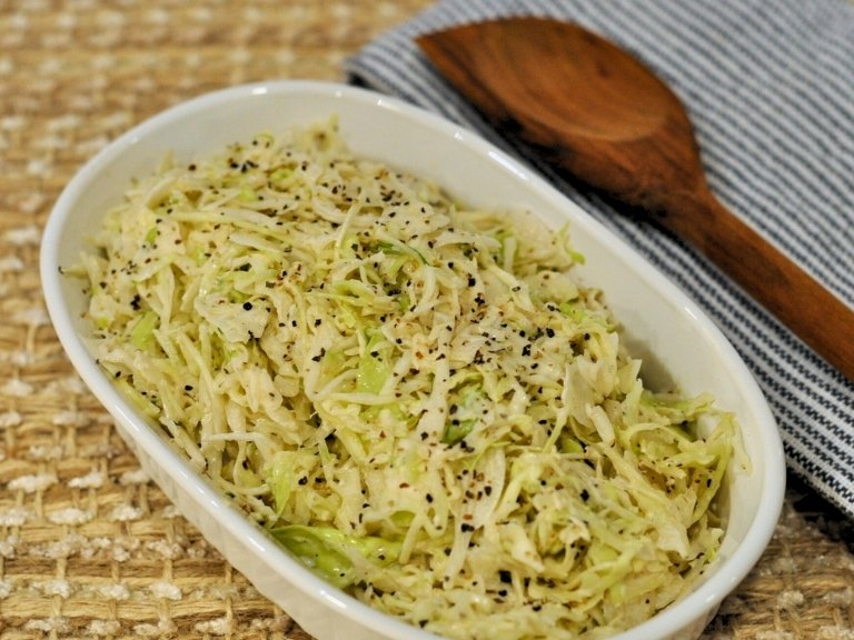 angel hair coleslaw in white bowl with wood spoon in background