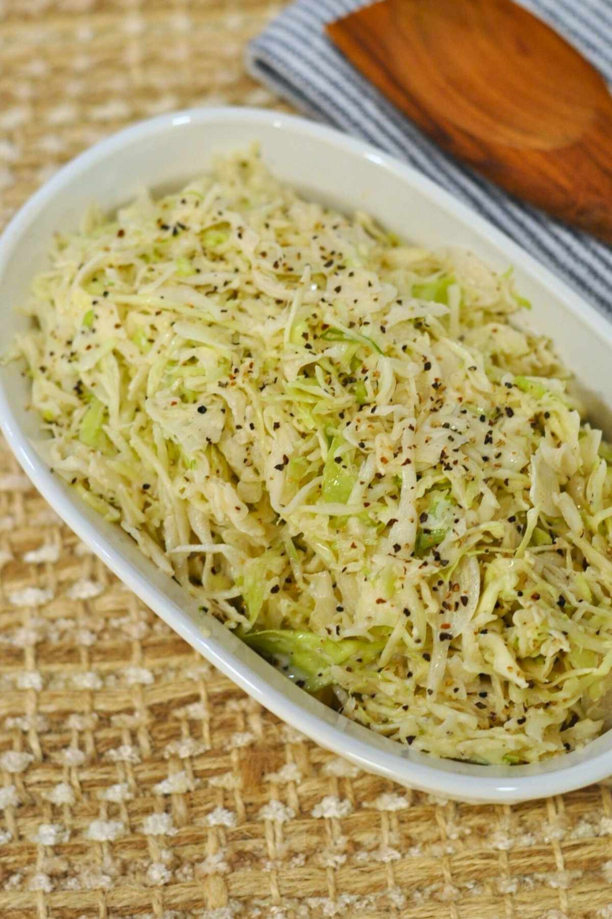 angel hair coleslaw in white bowl with wood spoon in background