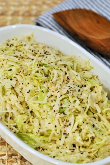 angel hair coleslaw in white bowl with wood spoon in background