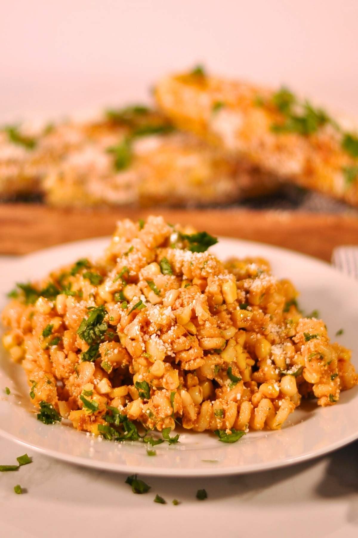 elotes pasta salad on white plate with three elotes in background