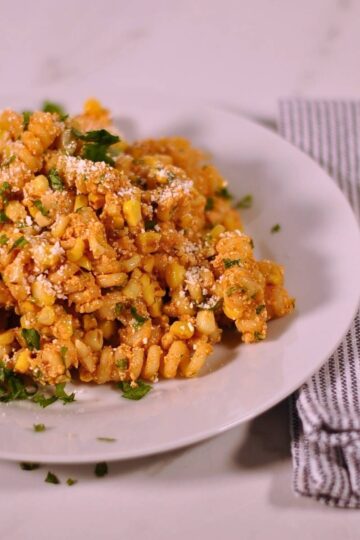 elotes pasta salad on white plate with fork sitting on blue and white napkin