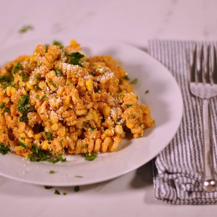 elotes pasta salad on white plate with fork sitting on blue and white napkin