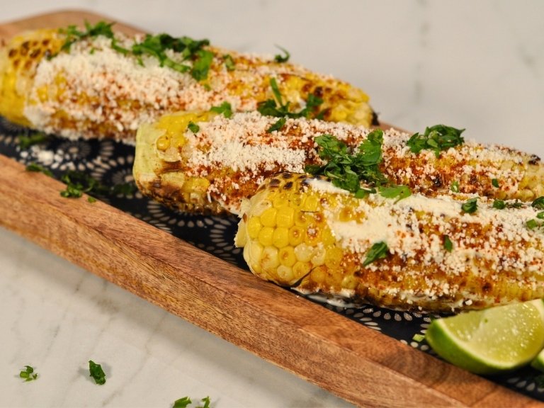 elotes (Mexican street corn) on wooden platter with lime wedge