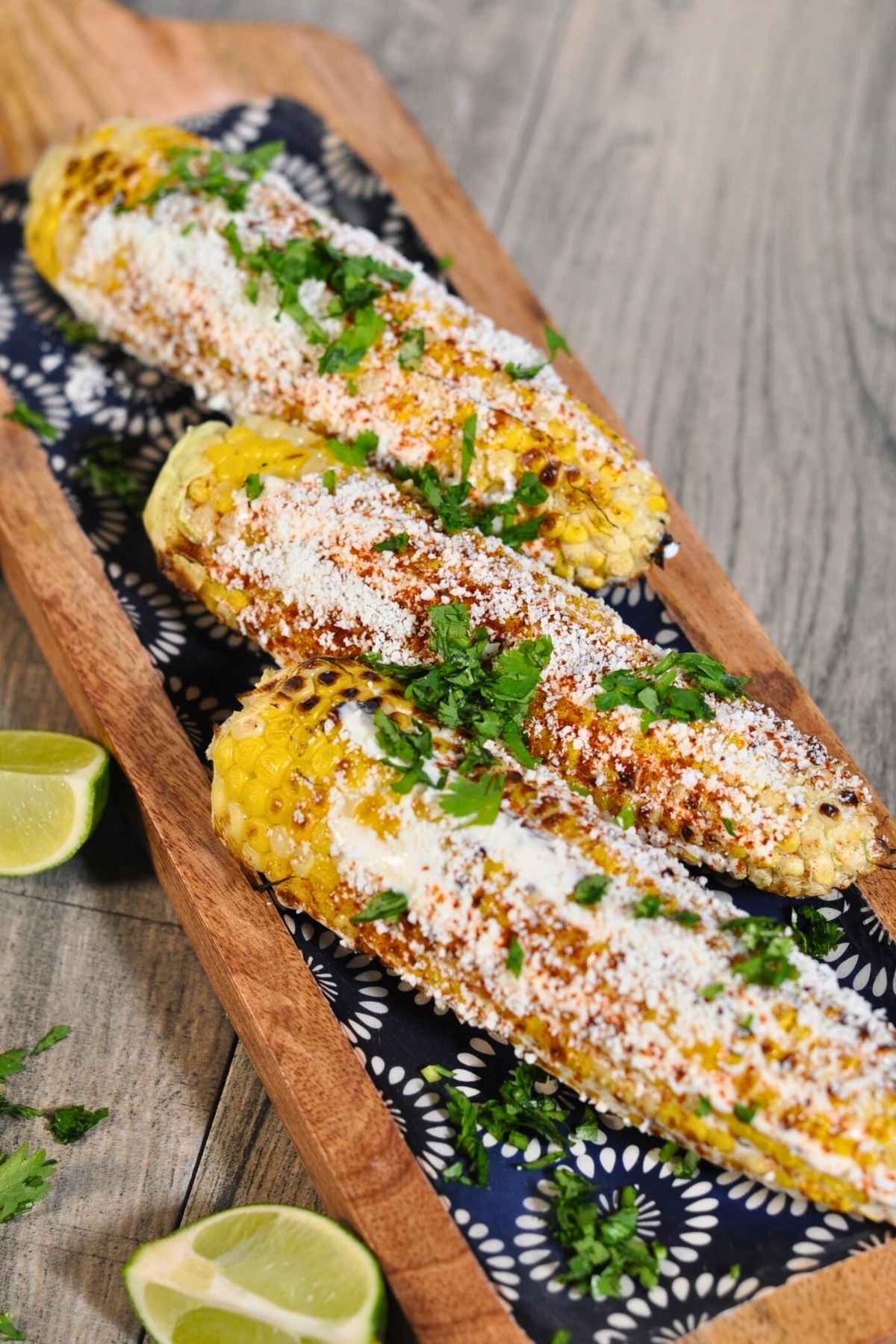 three elotes (Mexican street corn) on wooden blue plate with lime on the side