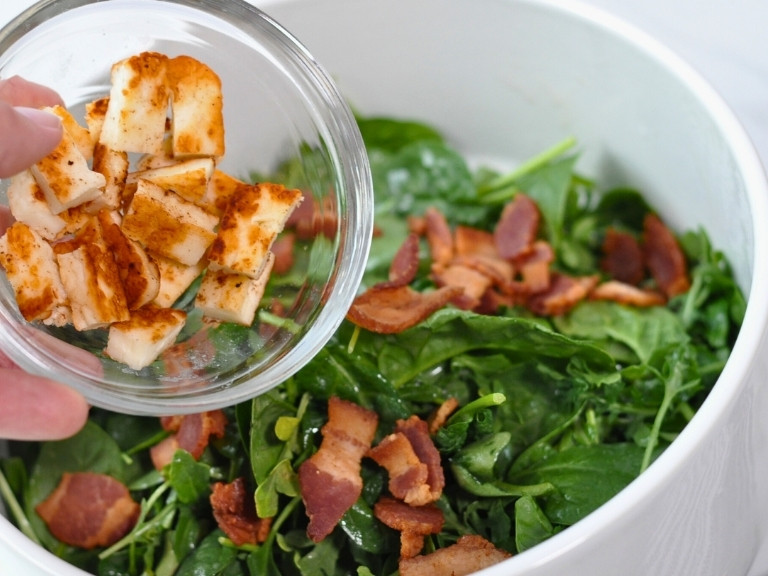 Arugula and Spinach Salad with bacon having grilled halloumi cheese being mixed in.