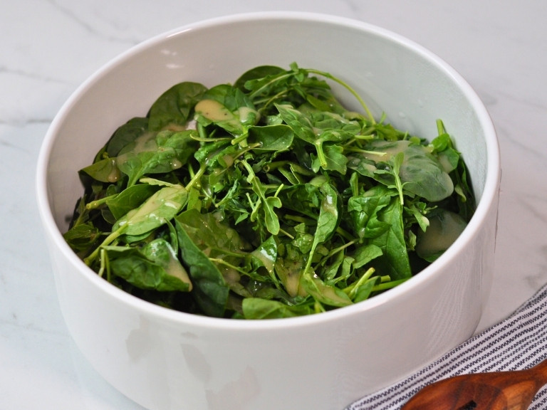 Arugula and Spinach and vinaigrette dressing in white salad bowl