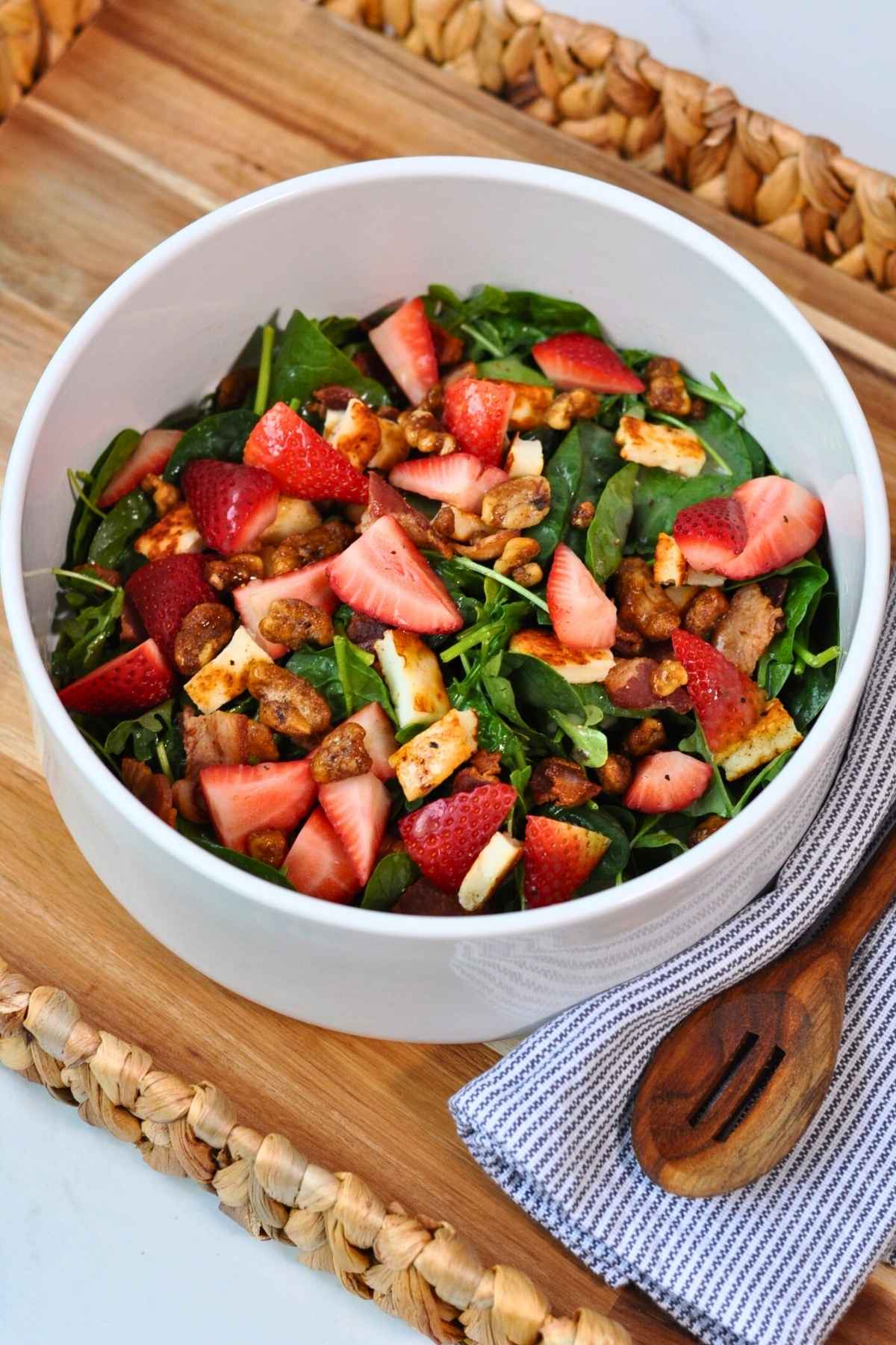 arugula and spinach salad in white bowl on wooden tray with blue and white napkin and wooden spoon