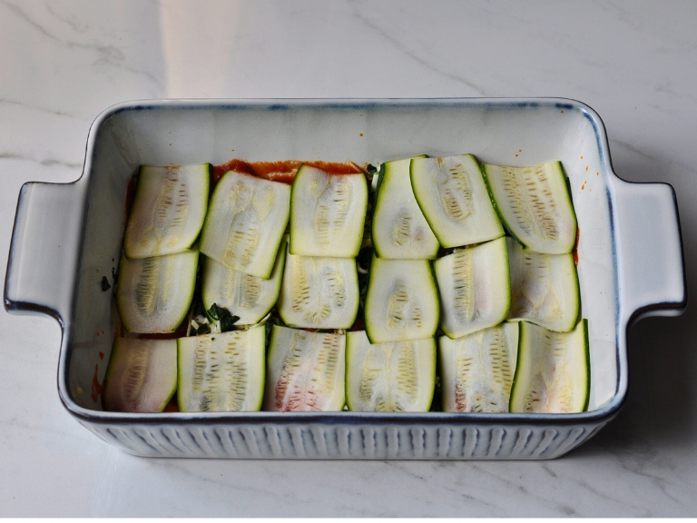 sliced zucchini and marinera sauce in white and blue baking dish