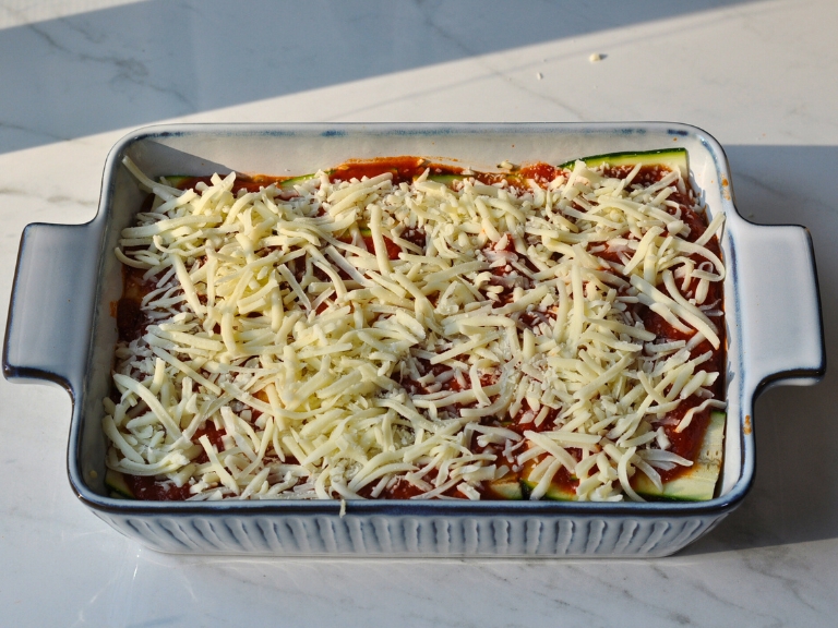 beef, spinach lasagna with zucchini slices topped with mozzarella cheese uncooked in baking dish