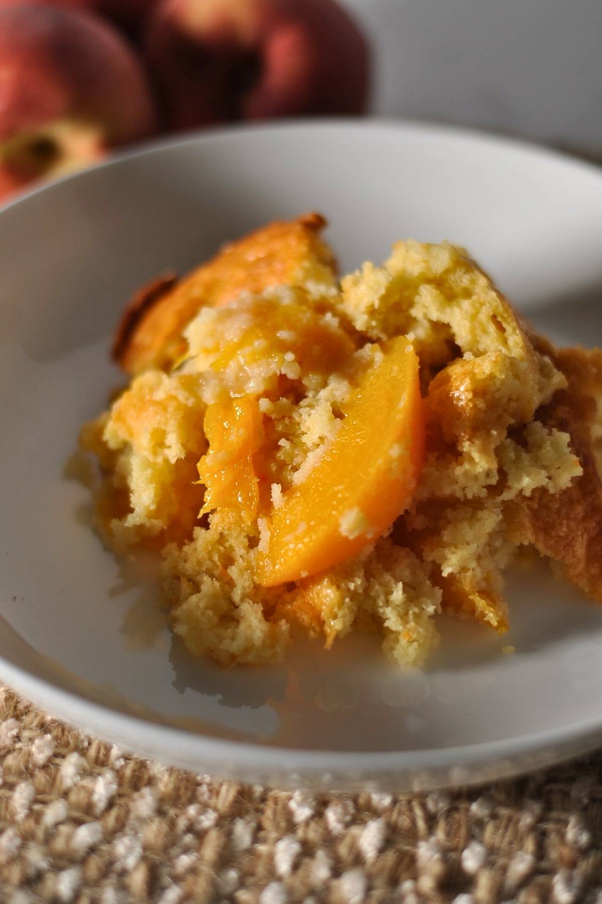 peach cobbler on a white plate with a whole peach in the background