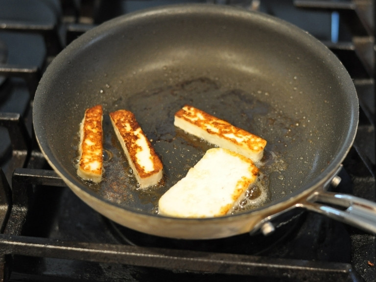 Halloumi cheese frying in a fry pan on top of stove