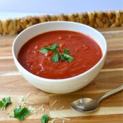 red marinara sauce in white bowl with green parsley on top, sitting on wooden tray with silver spoon.