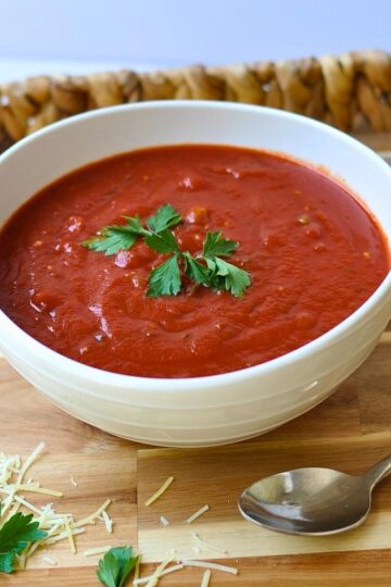 red marinara sauce in white bowl with green parsley on top, sitting on wooden tray with silver spoon.