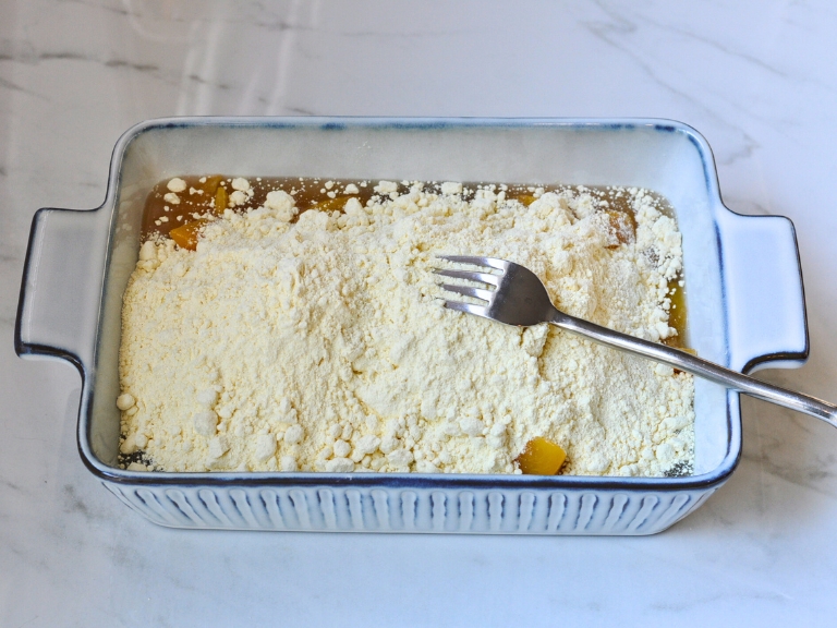 canned peaches and cake mix in a blue and white rectangle baking dish with silver fork on top of mix