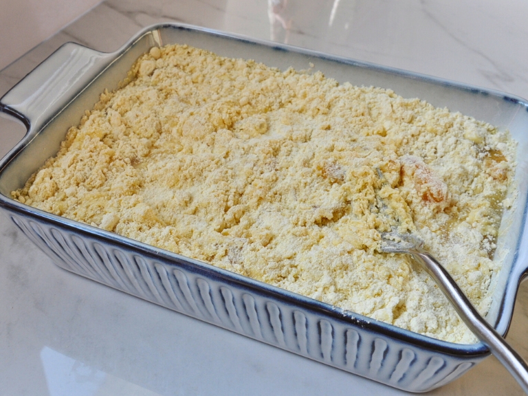 Cake mix and peached mixed together in baking dish with silver fork on top.