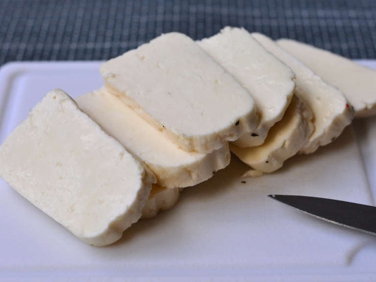 sliced Halloumi cheeses and paring knife on white cutting board.