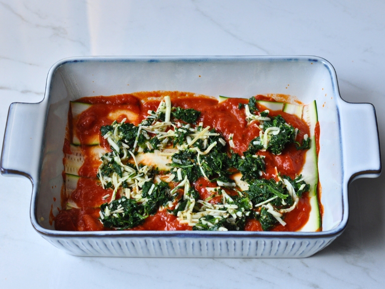 spinach, cheese, marinera sauce and sliced zucchini in blue and white baking dish