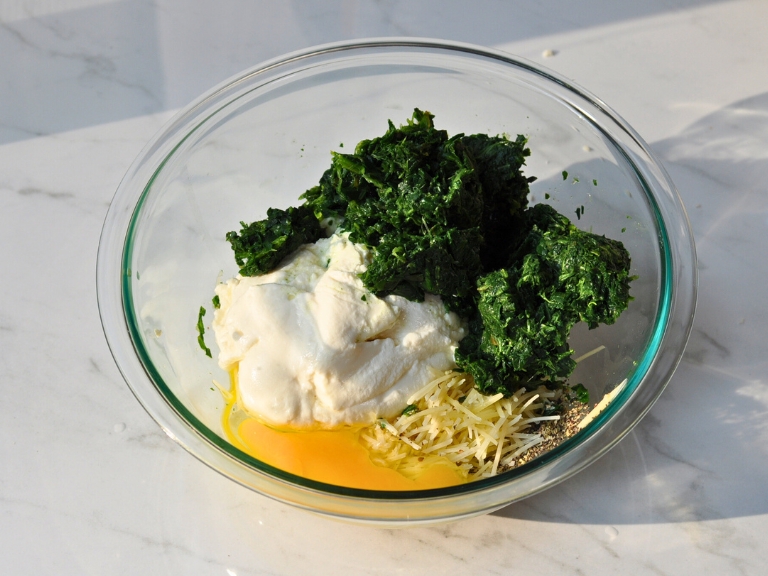 spinach, ricotta cheese, parmesan cheese, egg and seasonings in glass bowl on marble countertop